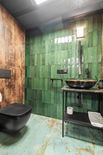 a green tiled bathroom with a black toilet and a sink at ALL - Amberstone Lux Loft in Klaipėda
