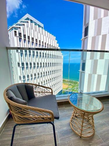a rattan chair and a glass table in front of a window at APEC Mandala Mũi Né in Mui Ne