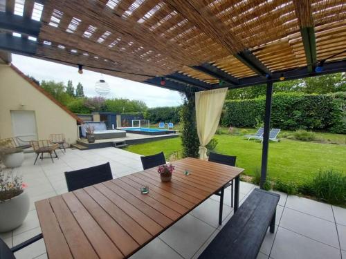 d'une terrasse avec une table et des chaises en bois sous une pergola. dans l'établissement Chambres des marais, à Merville-Franceville-Plage