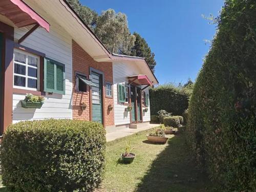 a house with green shutters and plants in a yard at Pousada Florada na Serra - Apto 1 in Campos do Jordão