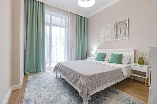 a white bedroom with a large bed with green curtains at Tokyo, a Residential Complex in Astana