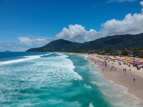 a group of people on a beach with the ocean at Flat Maresias in São Sebastião