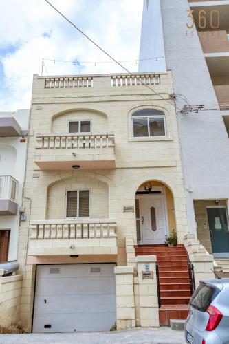 aige brick house with a balcony and a car parked in front at Spacious 4BR Terraced House with Rooftop Access by 360 Estates in Marsaskala
