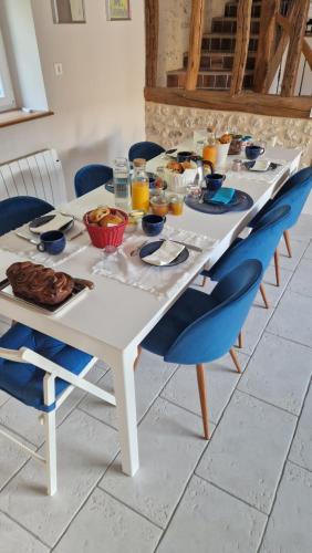 Una mesa blanca con sillas azules y comida encima. en La Maison Pas'Chaaxe, en Onzain