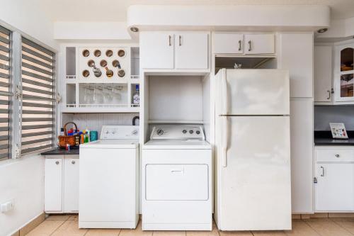 a kitchen with white cabinets and a refrigerator at ATOAS - Lovely Vacation Retreat with Pool and Barbecue 5 min to Boqueron and Beaches in Cabo Rojo