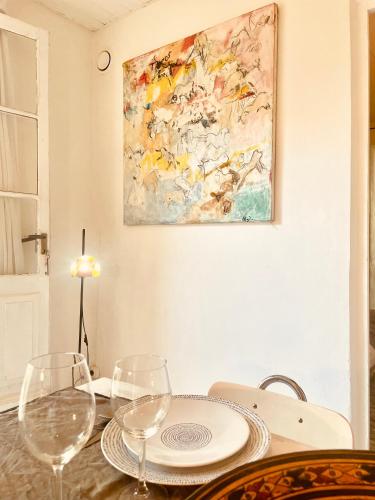 a table with two wine glasses and a painting on the wall at La Maisonnette du Parc - Piscine - Tennis in Nîmes