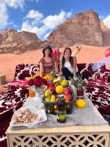 dos mujeres sentadas en una mesa con frutas y hortalizas en MOON RUM lUXURY CAMP, en Wadi Rum
