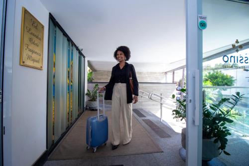 a woman walking down a hallway with a blue suitcase at Hotel Cassino Tower São José do Rio Preto by Nacional Inn in Sao Jose do Rio Preto