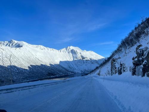 a snow covered road with a mountain in the background at FeelSenja Gryllefjord Holiday House in Gryllefjord