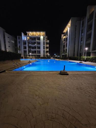 a large blue swimming pool at night with buildings at Grand hills in El Hamam
