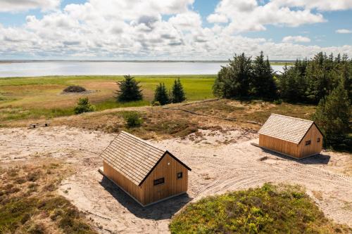 two small buildings on a field with a body of water at Bilberghus - Beyond Bed and Breakfast in Bjerregård