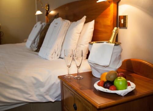 a bed with two wine glasses and fruit on a table at Warren Lodge in Shepperton