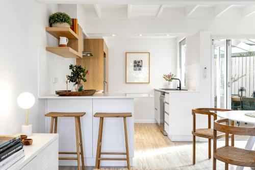 a kitchen with white counters and wooden stools at 2-Bed Coastal Haven with Pool by Sunshine Beach in Sunshine Beach
