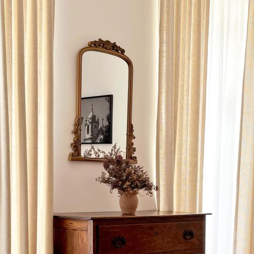 a mirror and a vase on a table with curtains at Senhora da Praça in Gavião