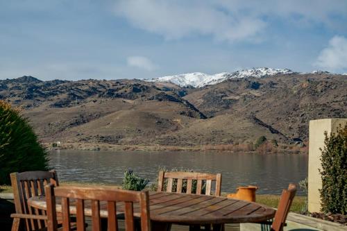 a wooden table and two chairs next to a lake at Mount Pisa Lake View in Cromwell