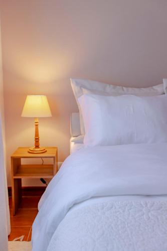 a bedroom with a white bed and a table with a lamp at Zur Suítes in Campos do Jordão
