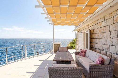 a balcony with a couch and tables and the ocean at Blue Views Villa with Heated Pool & Jacuzzi in Dubrovnik