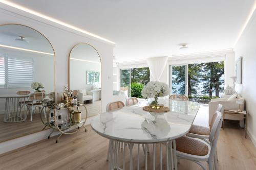 a white living room with a glass table and chairs at 3 Bedroom Beachfront Manly Garden Apartment in Sydney