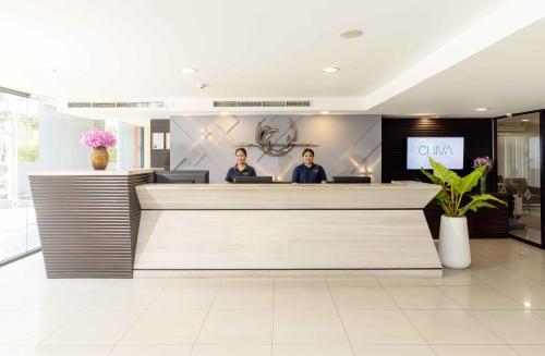 two people sitting at a reception desk in a lobby at Chiva Bangkok Hotel in Bangkok
