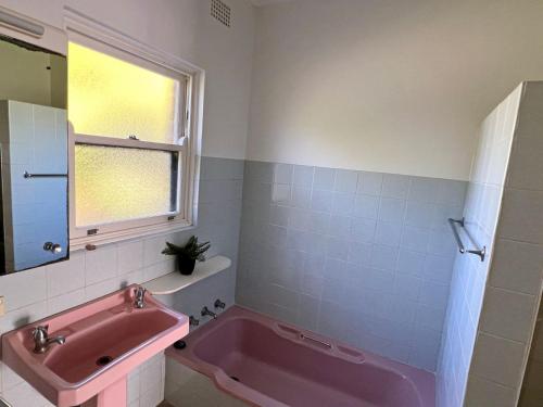 a bathroom with a pink tub and a window at Conns Cottage - Bring your own linen in South West Rocks