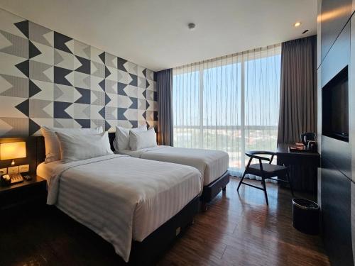 a hotel room with two beds and a desk and a television at Luminor Hotel Jemursari By WH in Surabaya