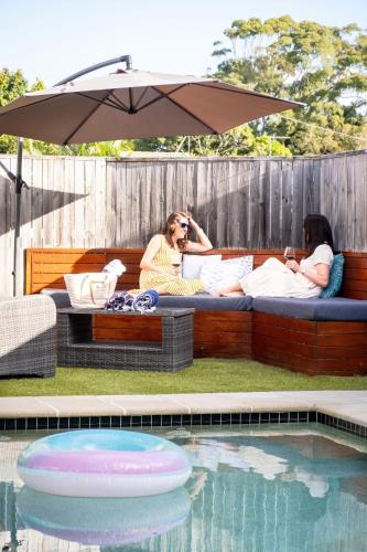 zwei Personen sitzen auf einem Bett unter einem Sonnenschirm neben einem Pool in der Unterkunft Kings Beach Home with Pool and Putt Putt in Caloundra