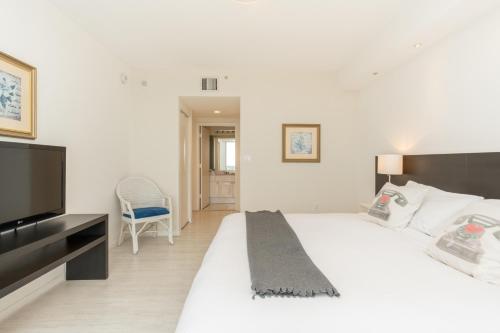 a bedroom with a white bed with a television and a chair at Golden Bay 1003 in Miami Beach