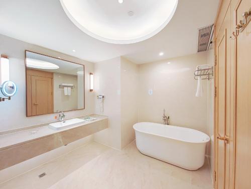 a bathroom with a tub and a sink and a mirror at Vienna International Hotel Wenchang in Wenchang