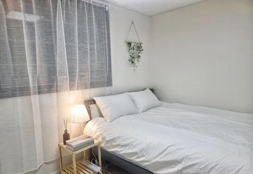 a white bedroom with a bed and a table with a lamp at Have Stay in Gumi