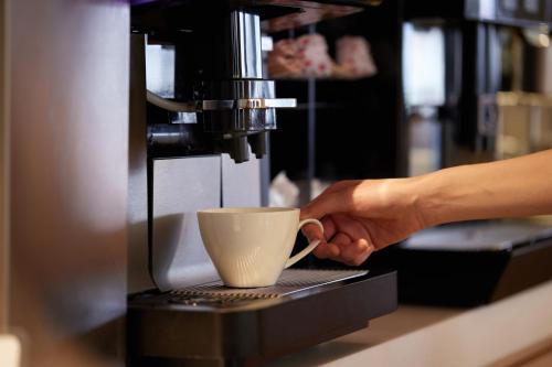a person making a cup of coffee in a espresso machine at Kobe Motomachi Tokyu REI Hotel in Kobe