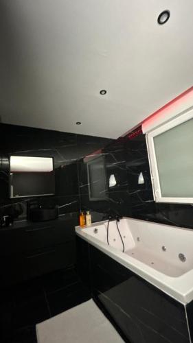 La salle de bains est pourvue d'une baignoire blanche et d'une fenêtre. dans l'établissement Black Room: Votre Love Room près de Lyon, à Vénissieux
