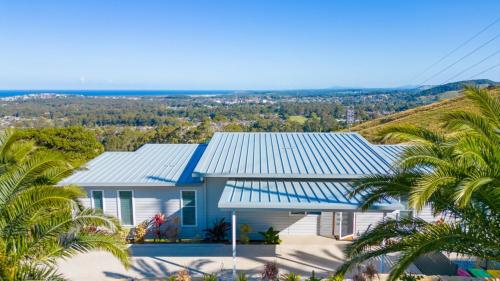 a house with a blue roof with palm trees at Altitude - Pet-Friendly, Romantic, Accessible in Coffs Harbour