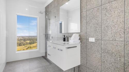 a white bathroom with a sink and a window at Altitude - Pet-Friendly, Romantic, Accessible in Coffs Harbour