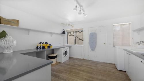a white kitchen with a sink and a washing machine at Barellen Beach House - Luxe Beach Front, Oceanview in Woolgoolga