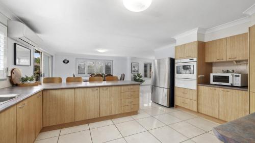 a kitchen with wooden cabinets and a stainless steel refrigerator at Chillax - Walk to Beach, Sauna, Pet-Friendly, Sleeps 6 in Coffs Harbour