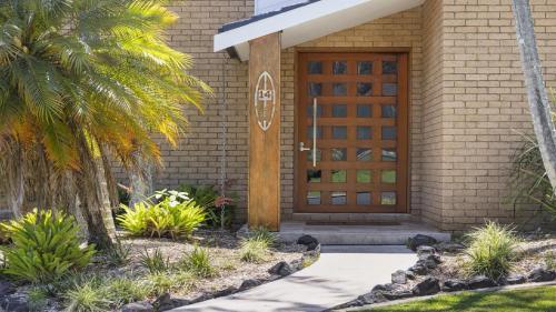 a front door of a house with a palm tree at Diggers Beach Surf House - Pool, Surf Beach, Pets, Sleeps 10 in Coffs Harbour