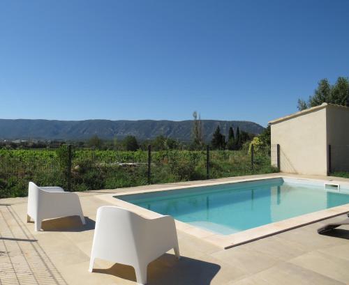 - une piscine avec 2 chaises blanches à côté dans l'établissement Maison face au Luberon avec piscine - 5 Chambres, à Cabrières-dʼAvignon