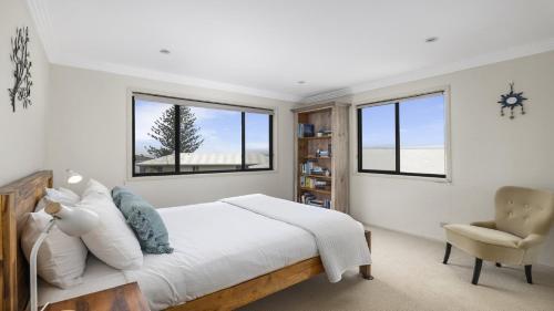 a bedroom with a bed and a chair and windows at Lighthouse at Emerald Beach - Ocean Views, walk to beach in Emerald Beach