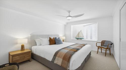a white bedroom with a bed and a chair at Lindy Lou's - Village at Doorstep, Restaurants in Sawtell