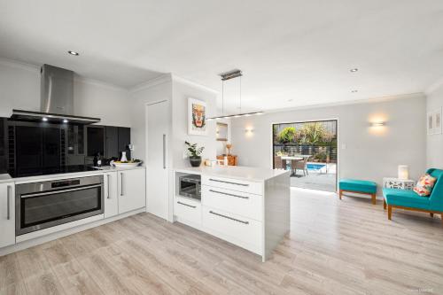 a kitchen with white cabinets and a living room at Villa with Pool in Browns Bay in Auckland