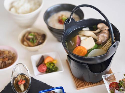 una pentola di cibo su un tavolo con ciotole di cibo di Hotel Holistic Resort Wakayama a Taiji
