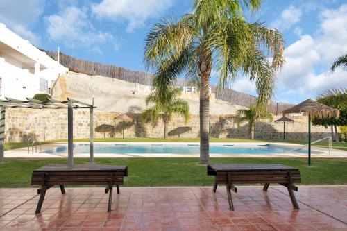 zwei Bänke vor einem Pool mit einer Palme in der Unterkunft Duplex marinero con vista al mar gimnasio piscina - LAS ABEJERAS 615 in Estepona