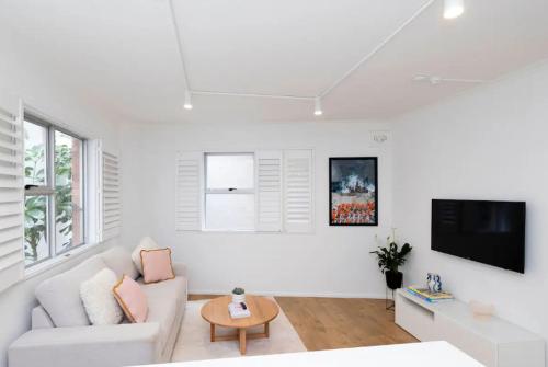 a white living room with a white couch and a tv at Beachside bright unit - sleeps 4! in Sydney