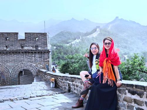 two women sitting on a wall at the great wall at Beijing Badaling Great Wall Caos Courtyard Hostel 1Private english tour guide 2Pick up&Drof off &landmark visiting serivice3Very near to Badaling Great Wall4Offer free beijing travel guide5Traditonal Chinese courtyard in Yanqing
