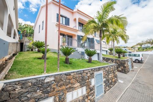 a house with palm trees and a stone wall at Atlantic Ocean Breeze in Ponta do Sol