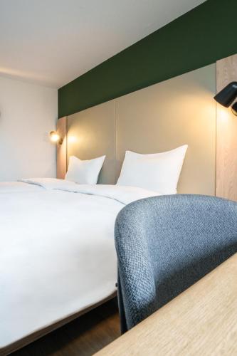 a bedroom with a large bed and a blue chair at Campanile NATURE - Bordeaux Sud Pessac in Pessac