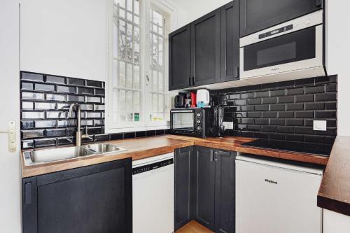 - une cuisine noire et blanche avec évier et four micro-ondes dans l'établissement Luxurious apartment - 3BR-6P - Nation, à Paris