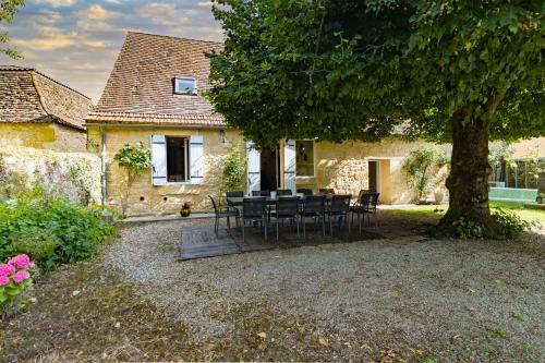 a table and chairs under a tree in front of a house at Maison en pierre piscine clim in Varennes