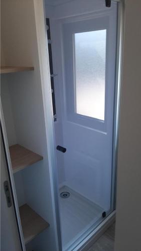 La salle de bains est pourvue d'une porte de douche en verre et d'une fenêtre. dans l'établissement Bungalow M027 chez D&D, à Torreilles