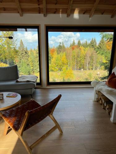a living room with a couch and a chair and large windows at Forestia - Modern cabin with hot tub and sauna in Dealu Negru